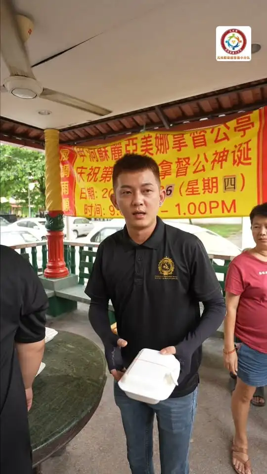 义工在组屋楼下的凉亭里，手上拿着一盒刚送到的饭盒